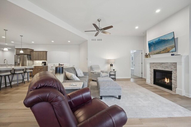 living area with light wood-type flooring, a stone fireplace, recessed lighting, visible vents, and ceiling fan