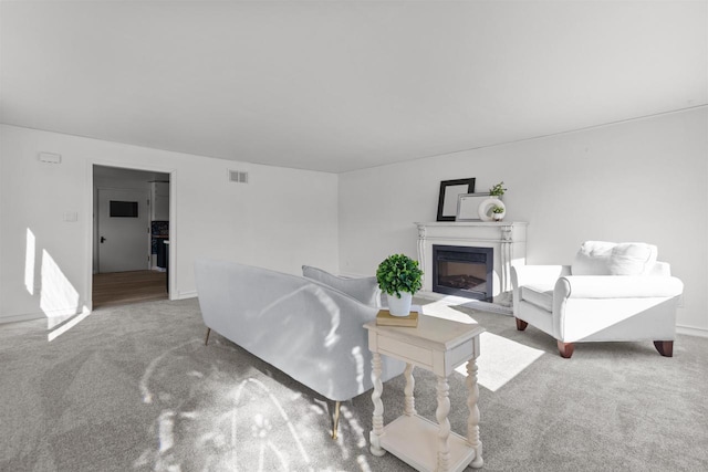 carpeted living room with a glass covered fireplace, visible vents, and baseboards