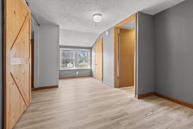 interior space featuring vaulted ceiling, light wood-style floors, a textured ceiling, and baseboards