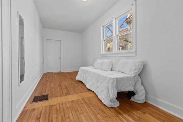 bedroom featuring light wood-style floors, visible vents, baseboards, and ornamental molding