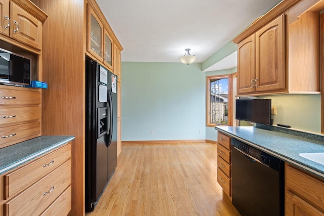 kitchen featuring baseboards, glass insert cabinets, dark countertops, light wood finished floors, and black appliances
