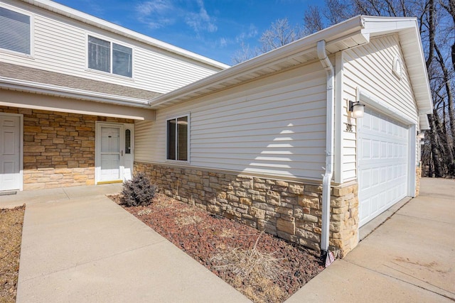 view of exterior entry featuring an attached garage, driveway, and stone siding
