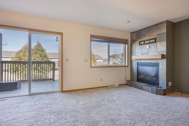 unfurnished living room featuring a tiled fireplace, baseboards, visible vents, and carpet floors