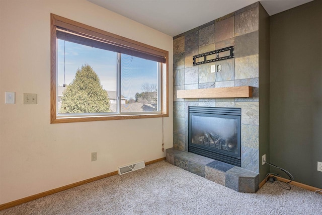 carpeted living room with baseboards, a tiled fireplace, visible vents, and plenty of natural light