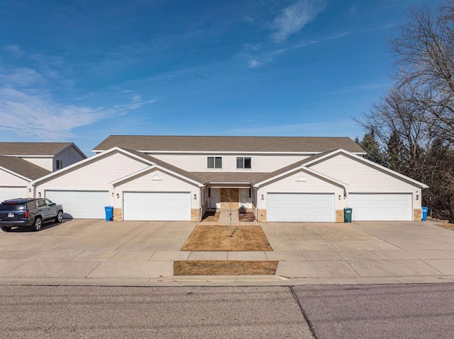 view of front of property featuring an attached garage, roof with shingles, concrete driveway, and stone siding