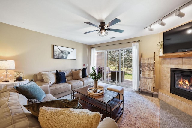 carpeted living room featuring visible vents, ceiling fan, a tiled fireplace, and track lighting