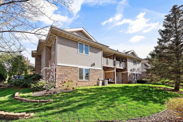 back of property featuring a lawn, brick siding, cooling unit, and a balcony