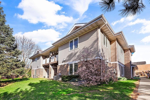view of side of home with brick siding, central AC unit, a lawn, and a balcony