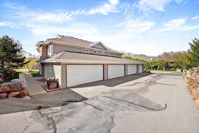 view of side of property featuring a shingled roof and community garages