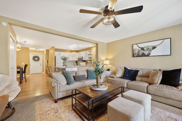 living room with a ceiling fan, baseboards, and light wood-type flooring