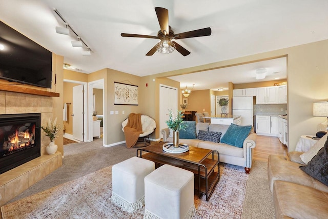 living area featuring a ceiling fan, light colored carpet, a tiled fireplace, track lighting, and baseboards
