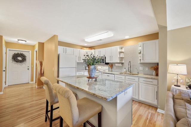kitchen featuring a kitchen breakfast bar, tasteful backsplash, a sink, white appliances, and white cabinetry