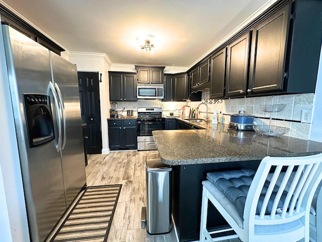 kitchen with a peninsula, a kitchen bar, stainless steel appliances, light wood finished floors, and a sink