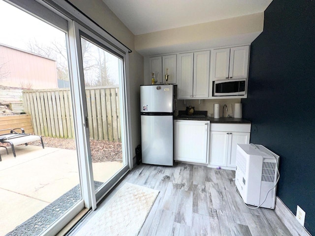 kitchen with light wood-style flooring, a sink, freestanding refrigerator, and dark countertops