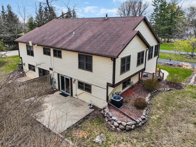 rear view of property featuring a patio area, roof with shingles, central air condition unit, and a lawn