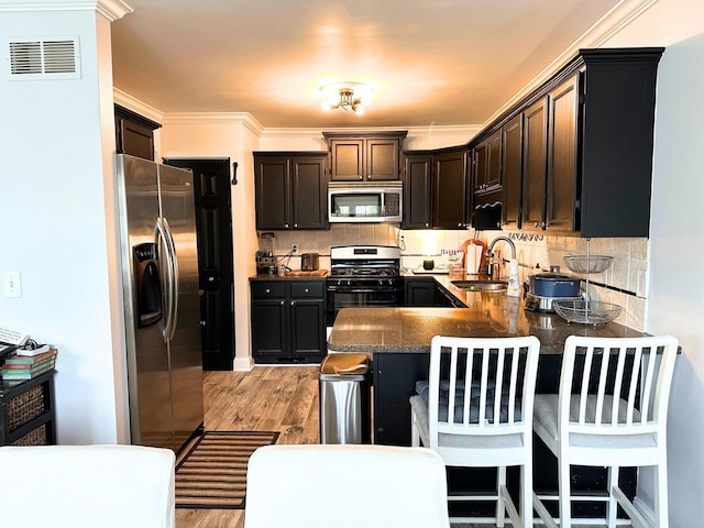 kitchen featuring visible vents, a sink, a peninsula, light wood finished floors, and stainless steel appliances