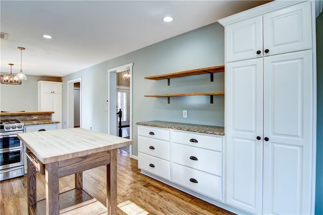 kitchen with an inviting chandelier, light stone counters, white cabinetry, light wood-style floors, and stainless steel range