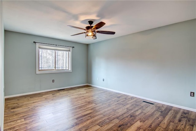 spare room with wood finished floors, baseboards, a ceiling fan, and visible vents