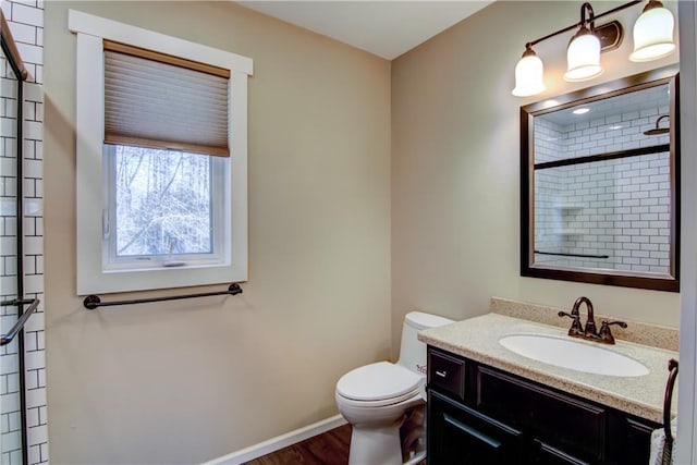 bathroom with baseboards, a tile shower, toilet, vanity, and wood finished floors