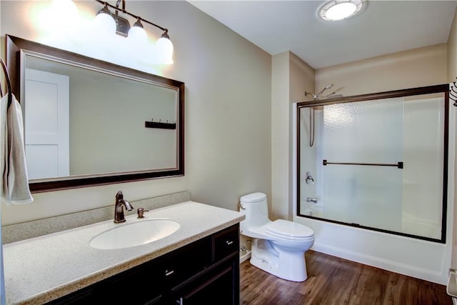 bathroom featuring toilet, enclosed tub / shower combo, vanity, and wood finished floors