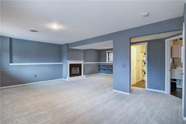 unfurnished living room featuring carpet flooring, baseboards, a glass covered fireplace, and visible vents