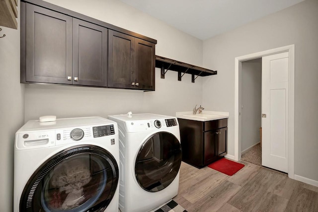 clothes washing area with light wood-type flooring, baseboards, independent washer and dryer, cabinet space, and a sink