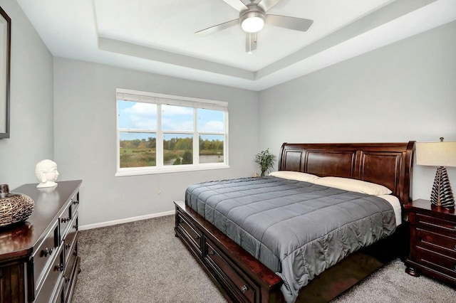 bedroom with a tray ceiling, baseboards, a ceiling fan, and light carpet