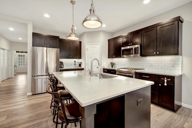 kitchen featuring dark brown cabinetry, a breakfast bar area, appliances with stainless steel finishes, light wood finished floors, and a sink