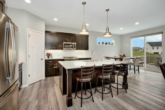 kitchen with a breakfast bar, light countertops, a sink, stainless steel appliances, and light wood finished floors