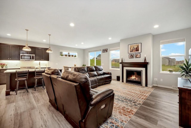 living area featuring a glass covered fireplace, recessed lighting, light wood-type flooring, and baseboards