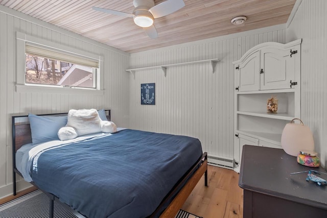 bedroom with wooden walls, light wood-style floors, a baseboard heating unit, and a ceiling fan