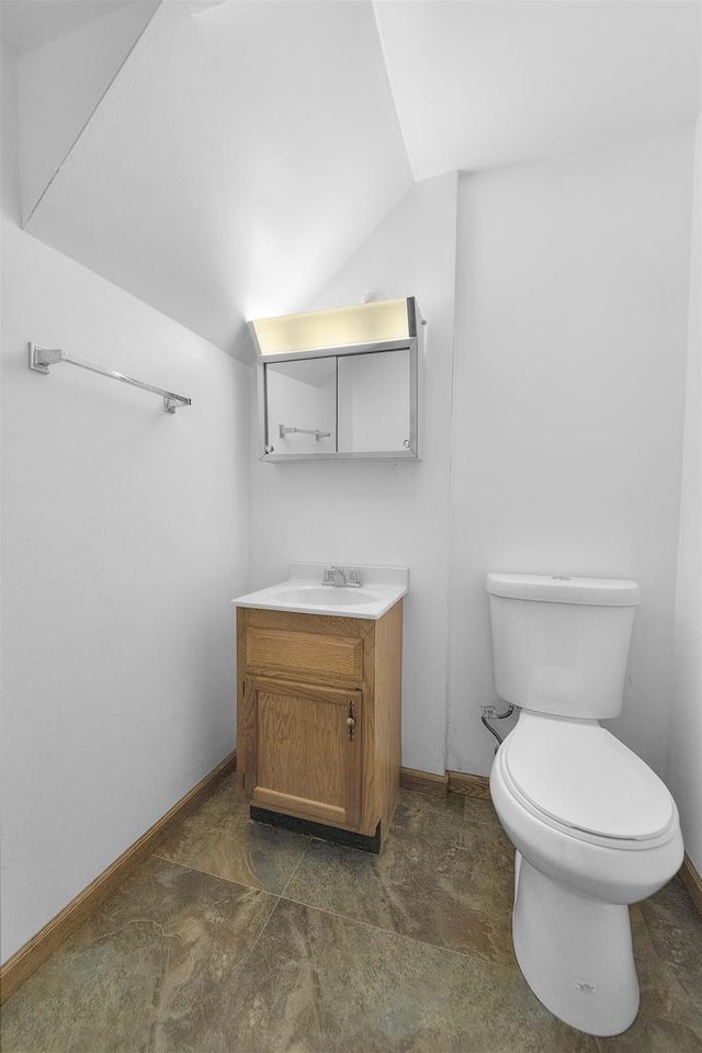 half bathroom featuring baseboards, toilet, lofted ceiling, and vanity