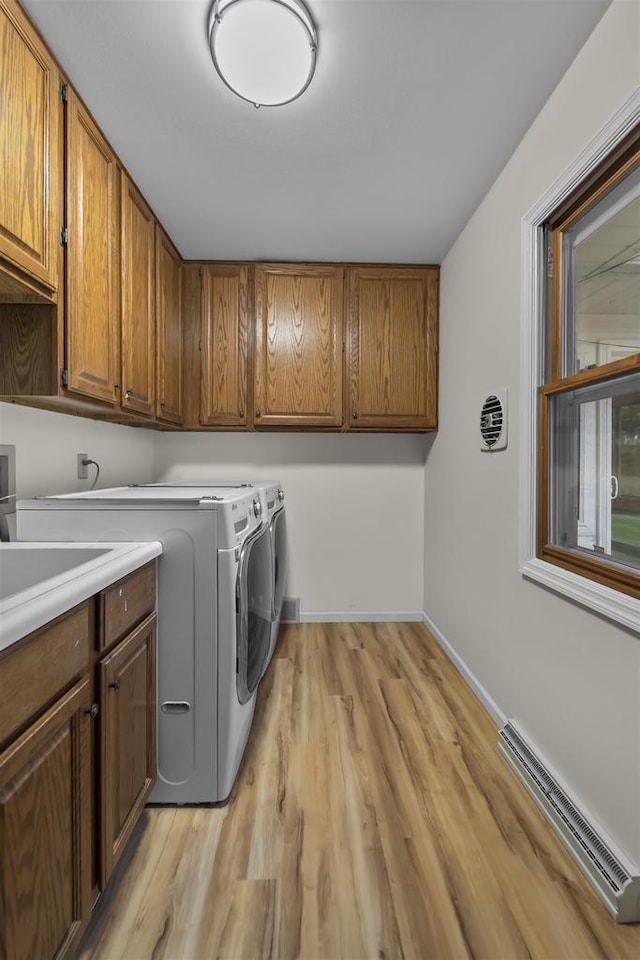 clothes washing area with independent washer and dryer, light wood-style flooring, visible vents, baseboards, and cabinet space