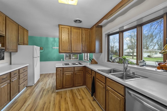 kitchen featuring a sink, brown cabinets, stainless steel appliances, light wood-style floors, and light countertops