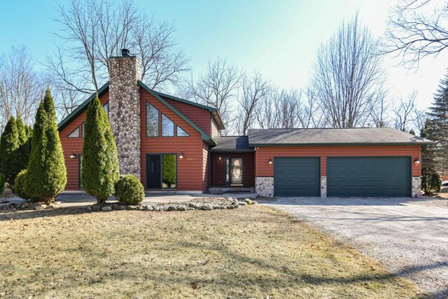 29323 Riverview Ln, Waterford, WI 53185 - view of front of house featuring a chimney, stone siding, log veneer siding, aphalt driveway, and a garage