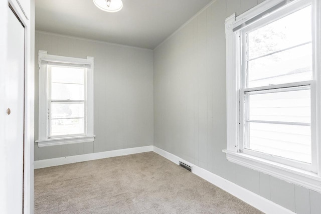empty room with crown molding, visible vents, baseboards, and carpet