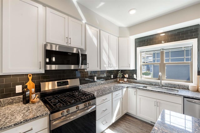 kitchen with light stone counters, stainless steel appliances, white cabinets, and a sink