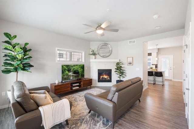 living area with a tile fireplace, a ceiling fan, visible vents, baseboards, and wood finished floors
