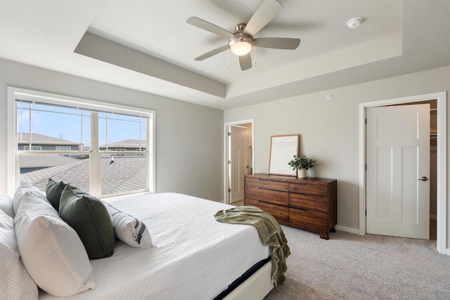 carpeted bedroom featuring a raised ceiling, a ceiling fan, and baseboards