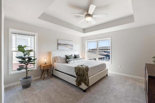 bedroom with baseboards, a raised ceiling, multiple windows, and light colored carpet