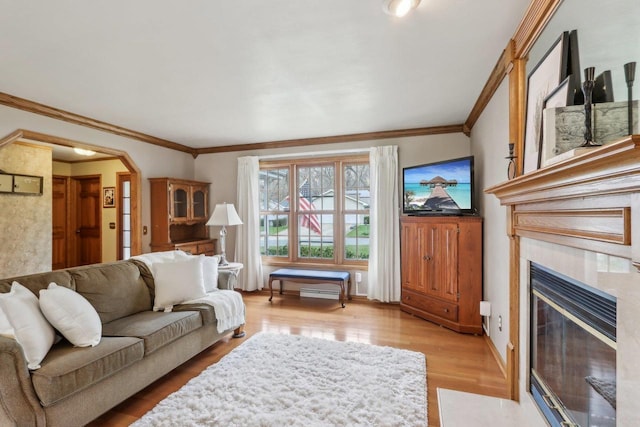 living room featuring a tiled fireplace, light wood-type flooring, ornamental molding, and arched walkways