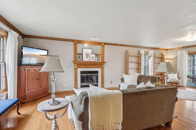 living area featuring crown molding, light wood finished floors, baseboards, and a glass covered fireplace
