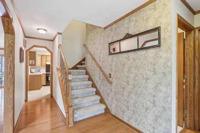 stairway featuring wood finished floors, baseboards, ornamental molding, and arched walkways