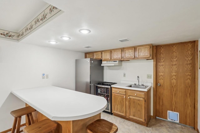 kitchen with under cabinet range hood, light countertops, a kitchen bar, a sink, and a peninsula