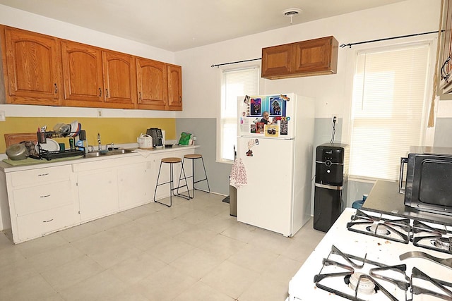 kitchen featuring freestanding refrigerator, black microwave, light countertops, a sink, and brown cabinets