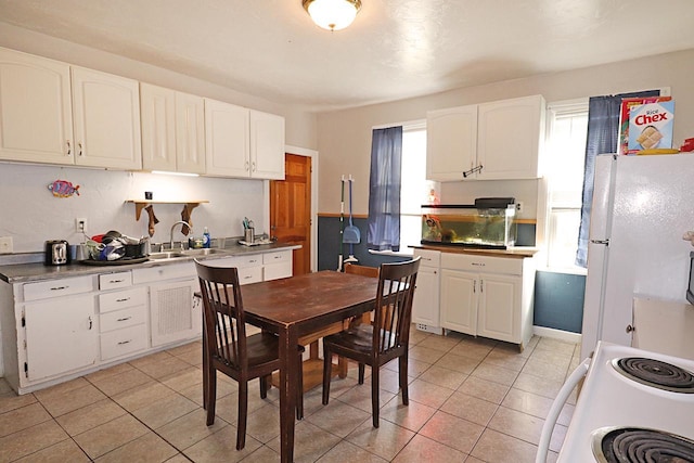 kitchen featuring light tile patterned floors, a sink, white appliances, and white cabinets