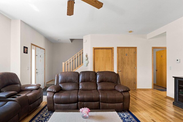 living area featuring a ceiling fan, baseboards, light wood-style flooring, and stairway