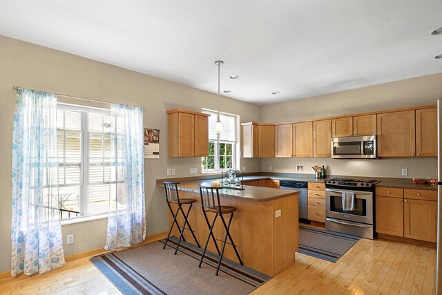 kitchen with a breakfast bar area, light wood-style flooring, stainless steel appliances, baseboards, and a peninsula
