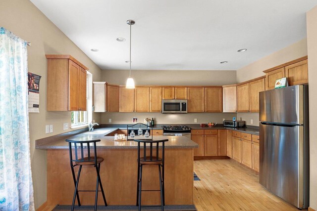 kitchen with a sink, light wood-style flooring, stainless steel appliances, decorative light fixtures, and a peninsula