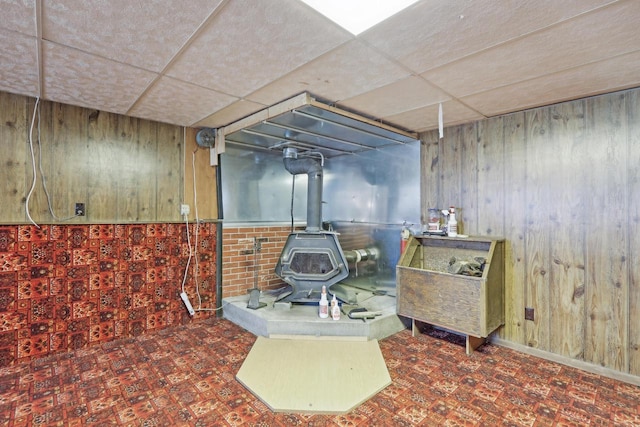 finished basement featuring wood walls, a paneled ceiling, and a wood stove